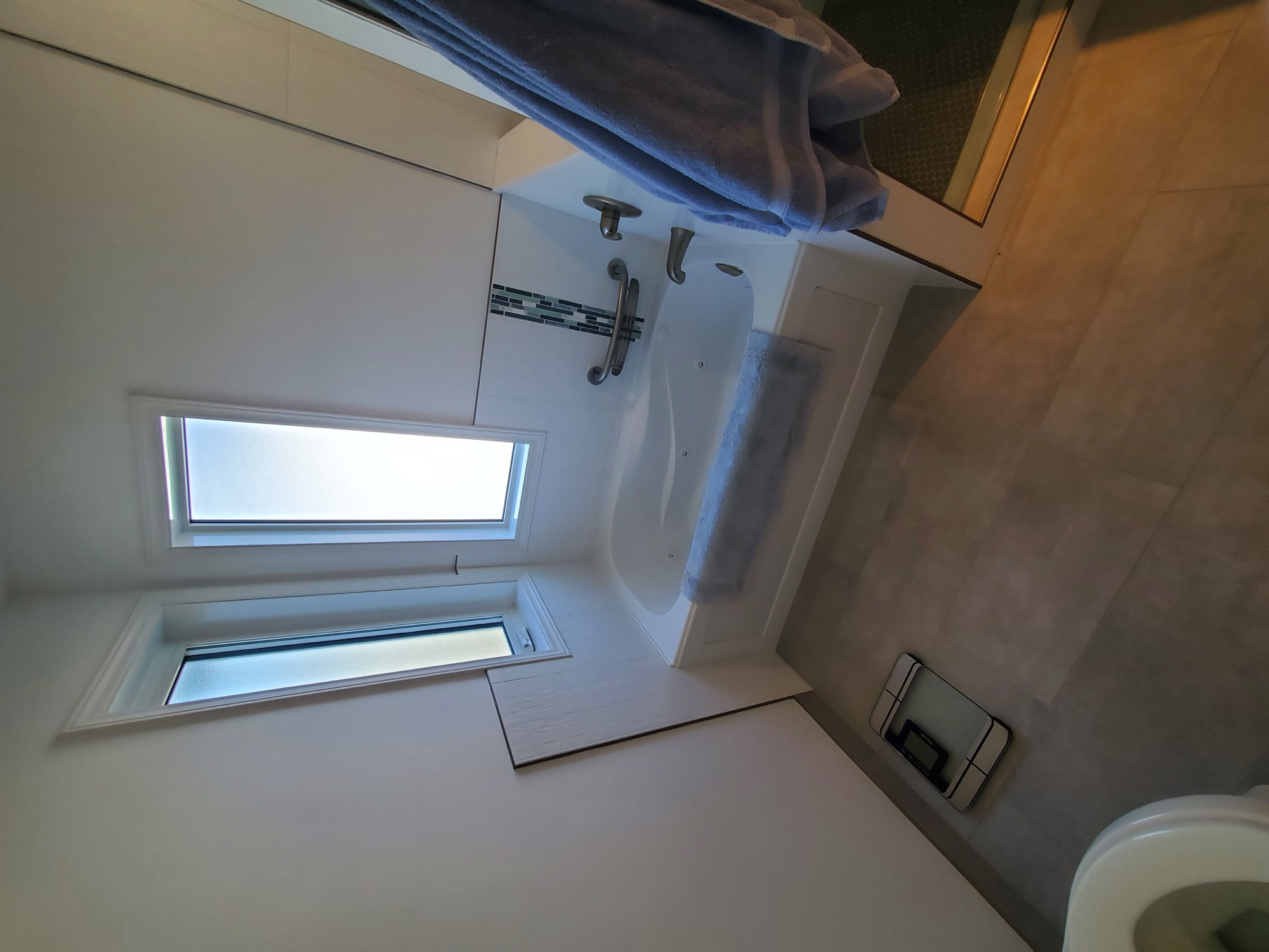 Tiled bathtub alcove with a glass mosaic accent strip beneath two windows