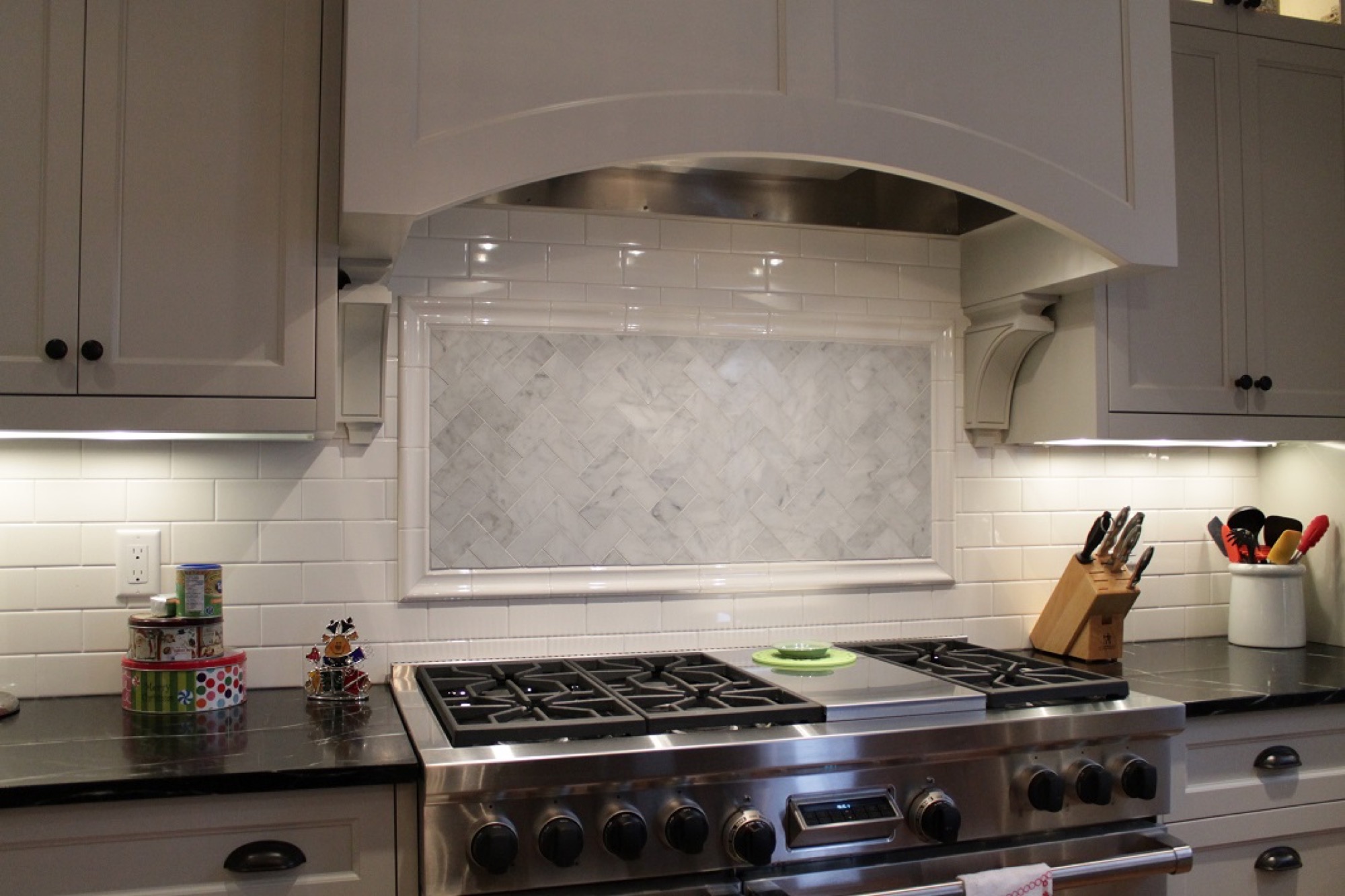 Marble mosaic backsplash panel behind a gas range under an arched range hood